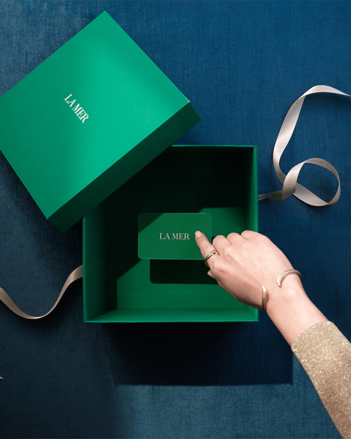 Gift Card in a La Mer Gift box with hand pointinga t it and a ribbon untied in the background.